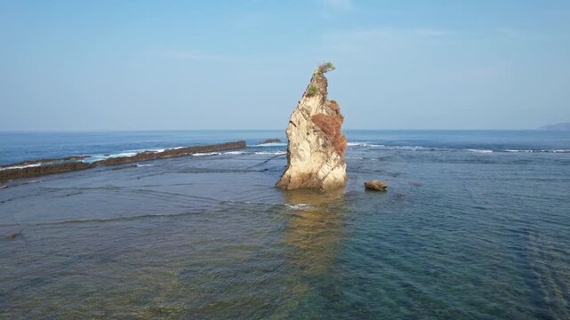 Aerial drone footage of around Tanjung Layar, a pointy rock formation in the middle of the rocky beach, with many waves hitting the reef, at sunrise, in Sawarna, Banten,south coast of Java, Indonesia