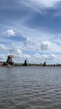 Windmills in Zaanse Schans historic village in the Netherlands. Famous traditional Dutch mills along the Zaan River in North Holland on a sunny and windy day.