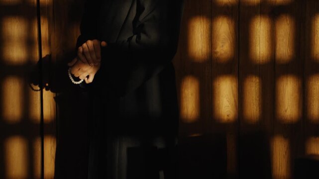 Priest praying with rosary in a dark confessional