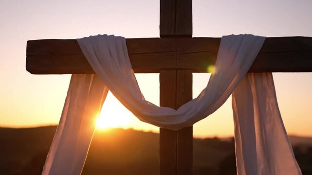 A wooden cross draped with a white burial cloth at sunset. Beautiful golden hour light symbolizing the resurrection of Jesus Christ and Easter morning.