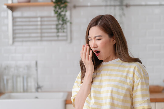 Young Asian woman is checking her breath by blowing into her hand. She feels insecure while checking for bad breath, showing a need for oral hygiene and dental care.