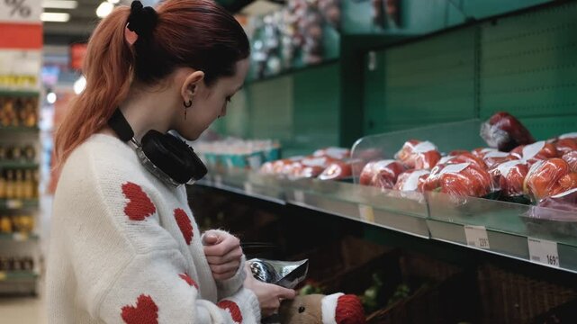 A young woman in a white wool sweater buys fruits at a supermarket in winter.