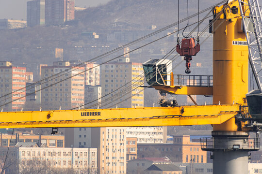 Vladivostok, Russia - February 14, 2026: Liebherr construction crane with yellow boom and city buildings in the background, showcasing urban industrial landscape