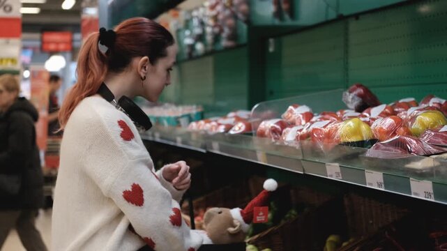 A young woman in a white wool sweater buys fruits at a supermarket in winter.