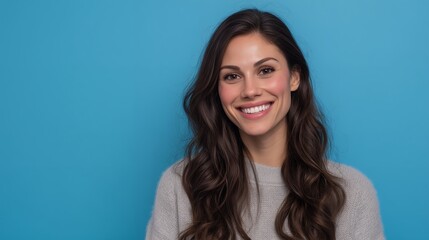 Fototapeta premium Portrait of a beautiful smiling marketing manager with long wavy hair against a plain blue background, concept for professional profile, corporate headshot and marketing campaign