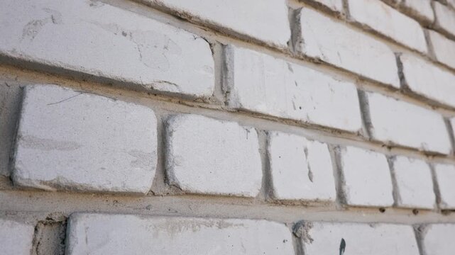 White brick wall surface viewed from a sharp angle highlighting the rough texture and gray mortar joints. Natural light casts subtle shadows across the painted masonry exterior.