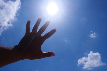 Reaching for the sun, a hand intercepts sunlight in a clear sky. The scene is both bright and uplifting.