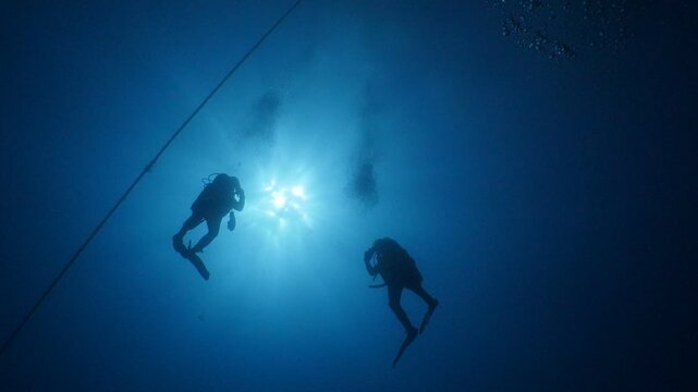scuba divers ascending surface going back to boat underwater with sun beams and rays ocean scenery