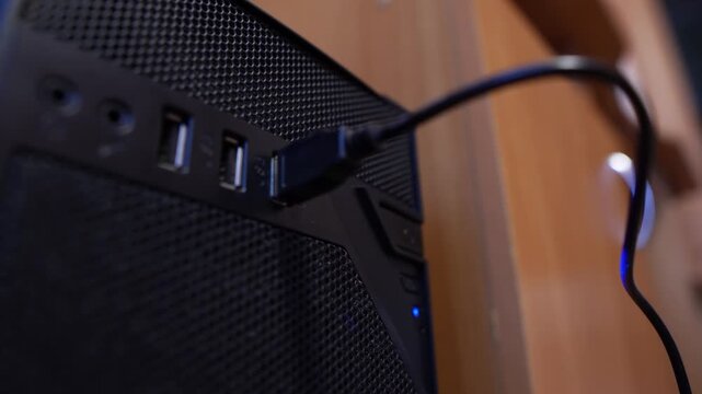A cord is inserted into a USB port on a computer in an office, close-up view