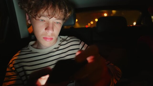 A young person sits in a car at night, illuminated by the glow of a mobile phone screen. They intensely use the device, eventually showing signs of discomfort or fatigue