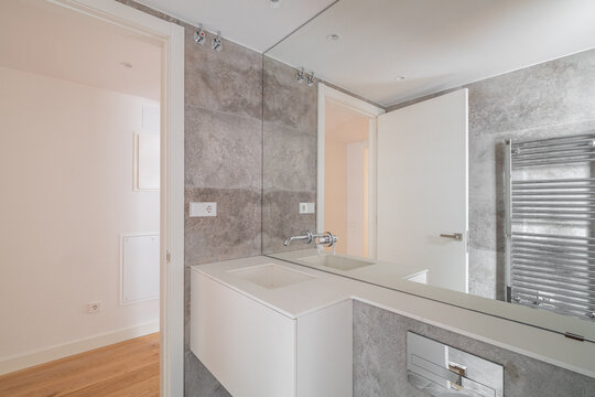 Modern bathroom with gray walls, a large mirror, and a sleek white sink. The space is well-lit and features a towel radiator.