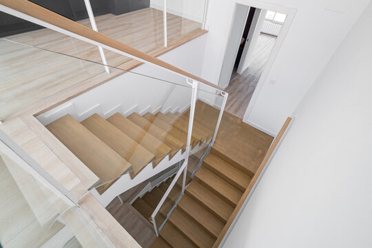 Modern staircase with wooden steps and glass railing in a bright interior. The design features clean lines and a minimalist aesthetic.