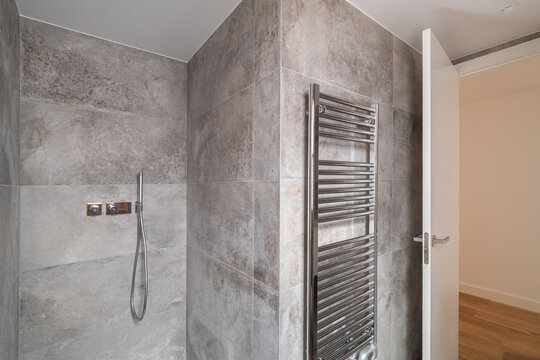 Modern bathroom with gray tiled walls, a shower with a handheld showerhead, and a heated towel rail. Bright and minimalistic design.