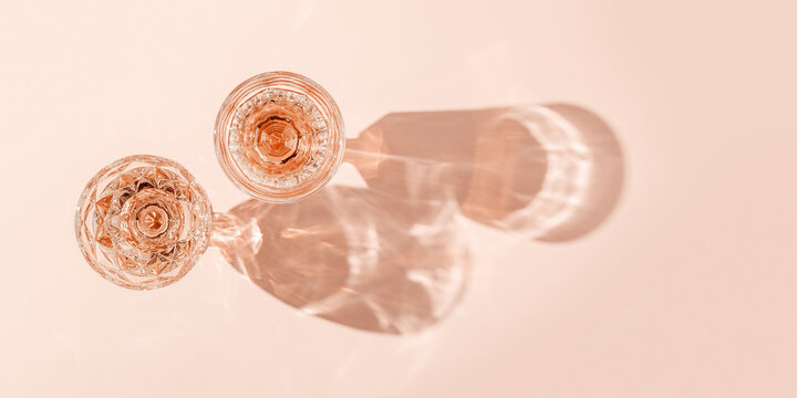 Top view two glasses of rose wine on peach color background, beautiful shadow at sun. Vintage wineglass minimal life style, close up sparkling alcohol drink, summer holiday mood, festive banner