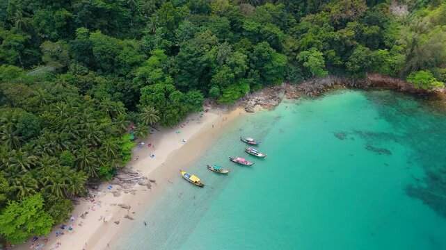 Aerial view of Banana Beach Phuket Thailand. Longtail boats rest in clear turquoise water while people relax on the sandy shore backed by tropical jungle