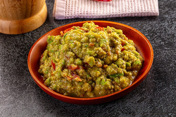 Freshly made guacamole dip with avocado and tomato in a rustic wooden bowl
