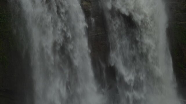 Close-up of powerful waterfall water curtain over dark rock and moss
