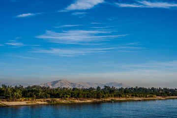 Fototapeta premium Riverbank with palm trees and distant mountains along the Nile