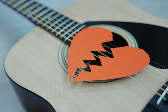 Broken red paper heart on acoustic guitar strings. Heartbreak playlist. Concept of heartbreak, emotional pain, breakup.