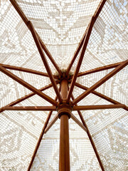 Looking up at a wooden umbrella with lace design during a sunny day