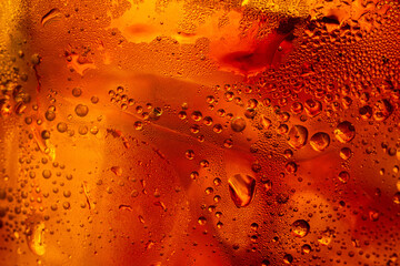 A close-up image of condensation droplets on a glass of refreshing amber-colored, cold cola drink,Macro shot of vibrant orange and red liquid texture behind a glass surface covered in fresh condensati © banjongseal324