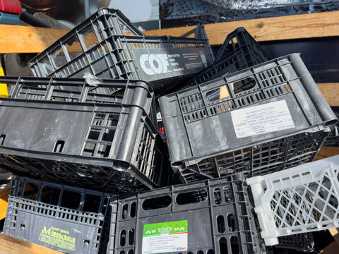 Villach, Austria - March 10, 2026: Stacked black plastic crates with various labels and logos on a wooden pallet in a storage area