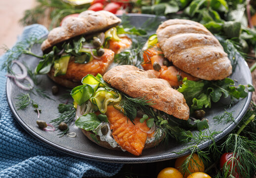 Salmon sandwich with veggies and yogurt sauce on a ceramic plate, close up view