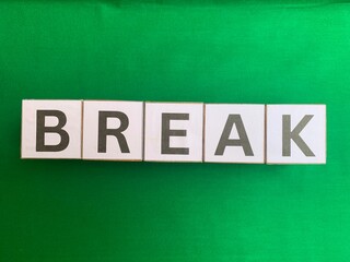 Obraz premium The word BREAK spelled out with white alphabet letter tiles on a solid bright green fabric background. Flat lay concept.