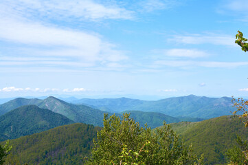 Fototapeta premium Panoramic view of lush green mountains under a clear blue sky with scattered white clouds in summer