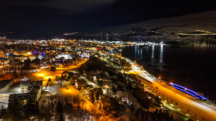 Obraz premium Drone view of Akureyri in North Iceland at night with illuminated bridge and city lights reflecting on water. Beautiful aerial scene of Akureyri harbor showing urban landscape and coastline in Iceland