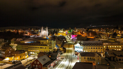 Fototapeta premium Drone view of Akureyri in North Iceland at night with illuminated bridge and city lights reflecting on water. Beautiful aerial scene of Akureyri harbor showing urban landscape and coastline in Iceland