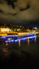 Fototapeta premium Drone view of Akureyri in North Iceland at night with illuminated bridge and city lights reflecting on water. Beautiful aerial scene of Akureyri harbor showing urban landscape and coastline in Iceland