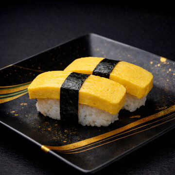 Premium fresh Japanese egg omelet tamago sushi on a luxury black ceramic plate with gold brushstrokes, dramatic lighting, high-end traditional Japanese cuisine.