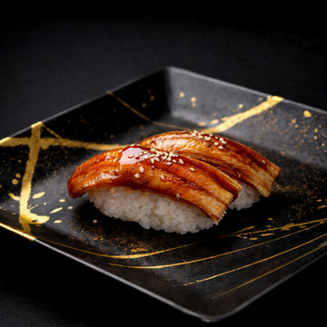 Premium fresh Japanese sea eel anago sushi with sweet sauce on a luxury black ceramic plate with gold brushstrokes, dramatic lighting, high-end traditional Japanese cuisine.