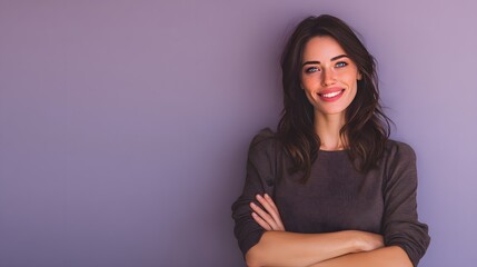 Fototapeta premium A confident woman with dark hair and a warm smile standing against a purple background with her arms crossed.