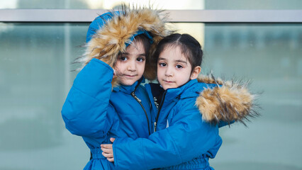 Adorable identical twin girls wearing warm blue winter parkas and hugging © Довидович Михаил