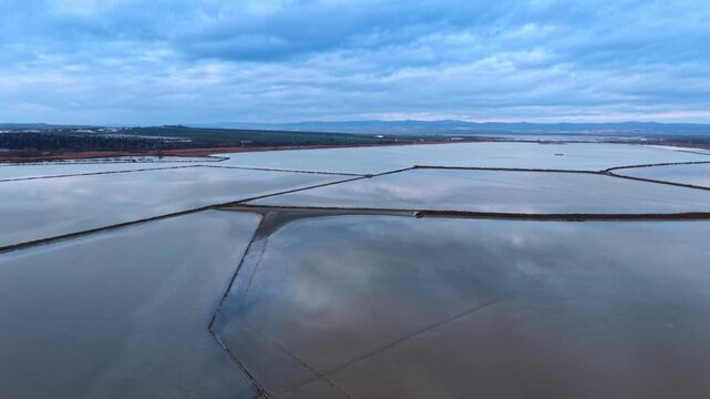 Vast pans with peaceful water reflecting cloudy sky. Salty ponds for salt crystallization for industrial production.