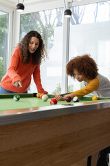Diverse female friends playing pool in bright game room with green felt table cues scattered balls