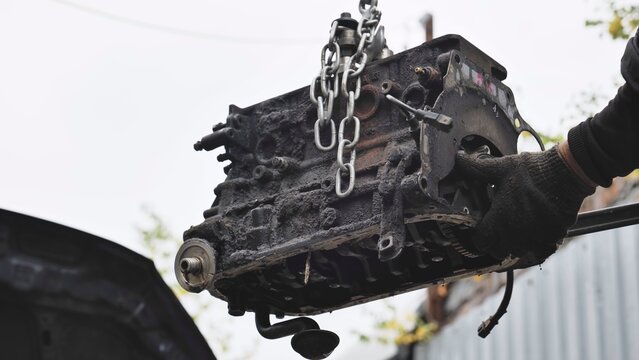 Mechanic pulling car engine block with chain hoist during vehicle maintenance