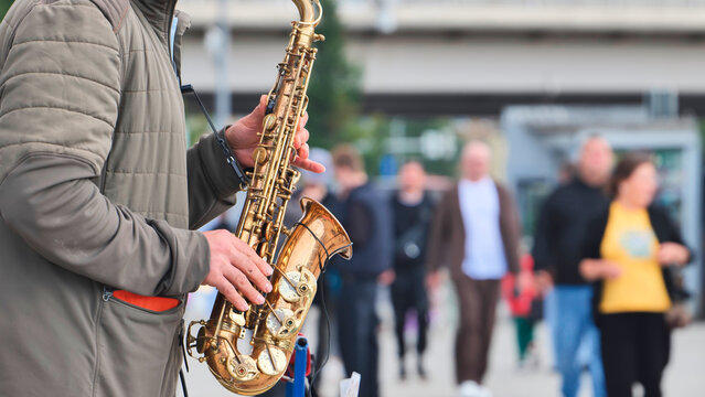 Street musician performing jazz music with a saxophone for passersby on a city sidewalk.