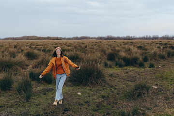 Young woman lifestyle walking outdoors in casual clothes on a field with grass and bushes. Autumn...