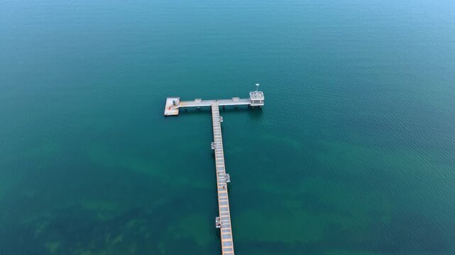 Pier over emerald green sea water top view. Aerial perspective of a wooden pier with small observation deck in calm sea.