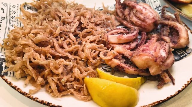 A plate of freshly fried elvers, young eels, served alongside crispy fried squid tentacles with lemon wedges in a seafood-specialized restaurant. Mediterranean seafood cuisine. High quality 4k footage