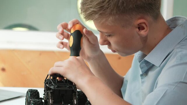 Close up of young student tighten the nut by using screwdriver. Caucasian teenager repairing or fixing car model while inspect robotic machine construction at STEM technology class. Edification