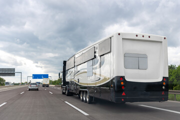 Large recreational vehicle camper trailer driving on highway under dramatic overcast cloudy sky during travel journey. Mobile motorhome transport used for vacation road trip tourism