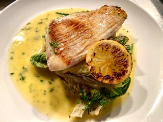Pan-fried skate wing fillet served with creamy lemon butter sauce, charred lemon, and seasonal greens on a white plate. Elegant seafood dish ideal for restaurant menus, fine dining, British cuisine,  © cheekylorns