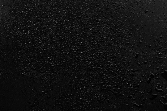 Water droplets on a black surface create patterns that catch light and shadows