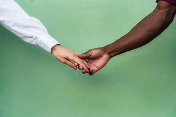 Interracial couple hands together, expressing partnership against a green background