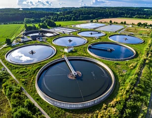 Elevated aerial of circular water treatment plant amidst green fields under a slightly cloudy sky © mahadewi