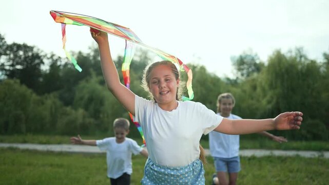 Children running outdoors playing. Group kids flying colorful kite. Happy children enjoy summer fun. Children playing outdoors in park. Children have joyful playtime. Group kids running and playing.